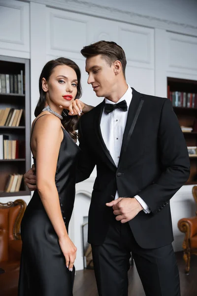 Elegant man in suit looking at girlfriend in silk dress at home — Stock Photo