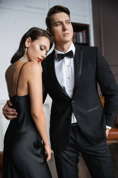 Elegant man in suit hugging brunette girlfriend in dress at home — Fotografia de Stock