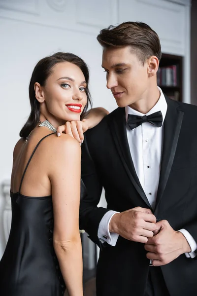 Smiling woman in dress looking at camera near elegant boyfriend at home — Photo de stock