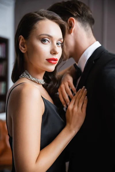 Elegant woman with red lips looking at camera near boyfriend at home — Stock Photo