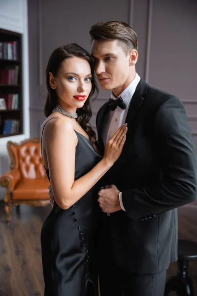 Smiling woman with red lips touching boyfriend in suit at home — Stock Photo
