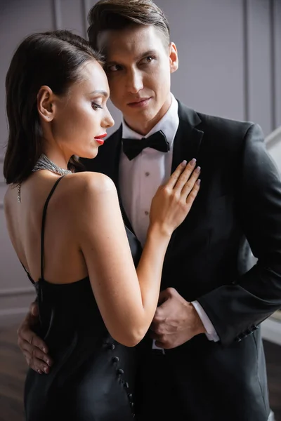 Brunette woman in dress touching boyfriend in formal wear at home — Fotografia de Stock