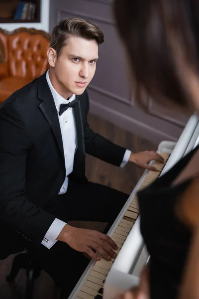 Elegant man in suit playing piano near blurred girlfriend at home — Stock Photo