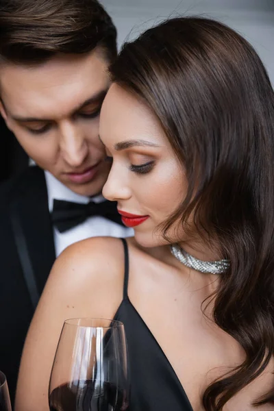 Brunette woman with red lips standing near boyfriend and glass of wine at home — Photo de stock