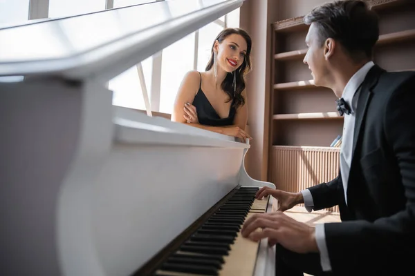 Smiling woman with red lips looking at elegant boyfriend playing piano at home — Stock Photo