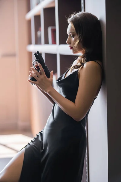 Side view of sensual woman in dress holding handgun at home — Stock Photo