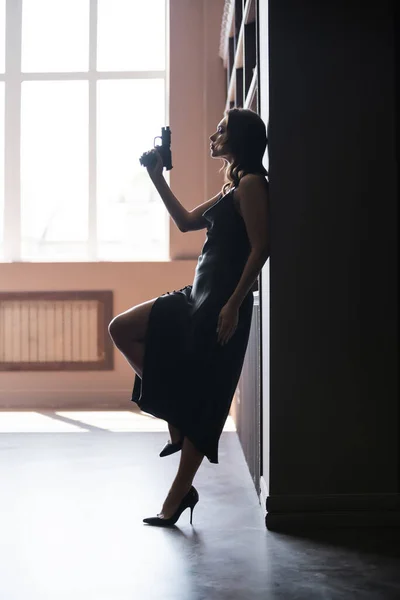 Side view of sensual woman in dress holding handgun at home — Stock Photo