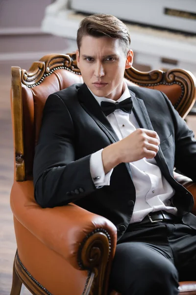 Portrait of elegant man in suit looking at camera while sitting on leather armchair at home — Stock Photo