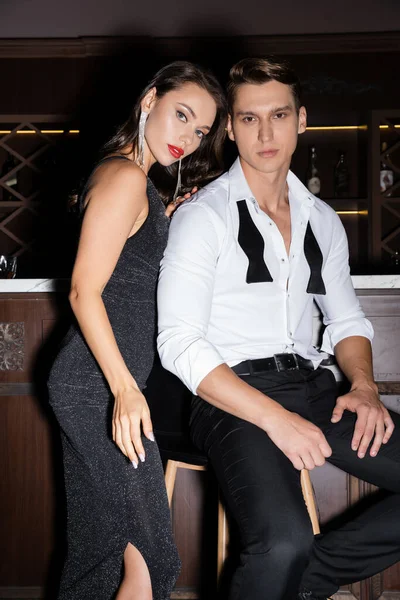 Seductive woman in dress looking at camera near elegant boyfriend in bar — Stockfoto