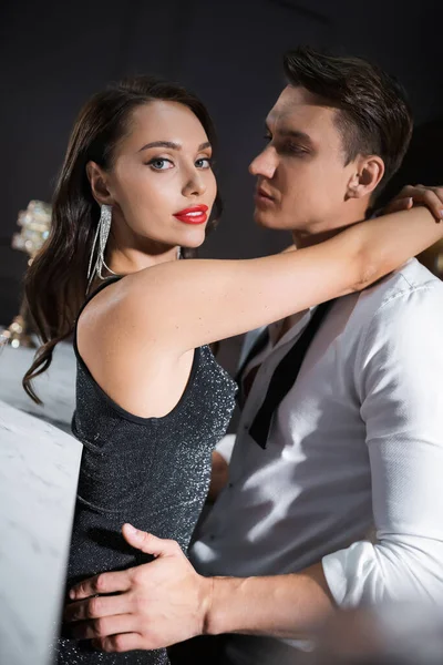 Seductive woman in dress embracing boyfriend in shirt and looking at camera at home — Photo de stock