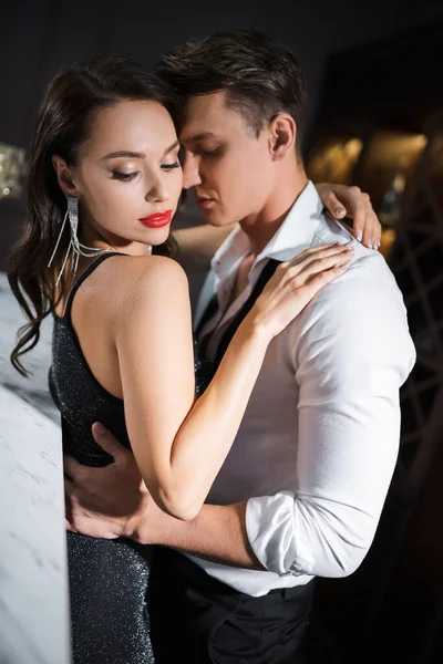 Elegant man in shirt hugging sensual girlfriend with red lips at home in evening — Stock Photo