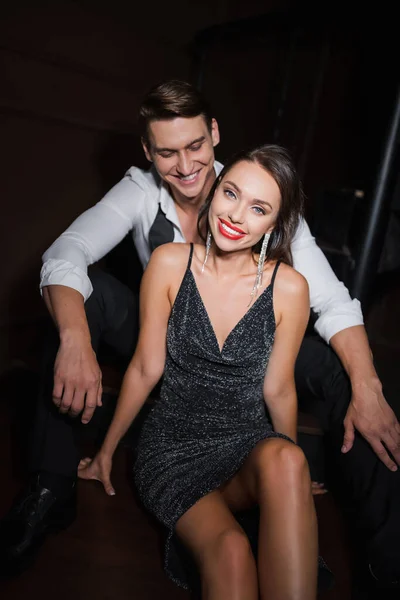 Smiling man in shirt looking at elegant girlfriend in dress at home in evening — Stock Photo