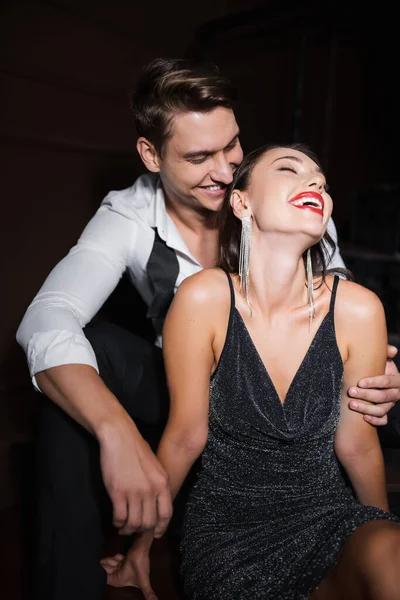Smiling man in shirt touching elegant girlfriend in dress at home in evening - foto de stock