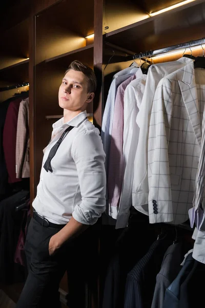 Elegant man looking at camera near shirts in cupboard in wardrobe — Stockfoto