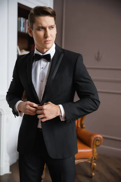 Elegant man buttoning jacket and looking away at home — Stock Photo