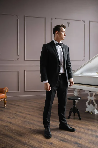 Elegant man in suit standing near piano at home — Stock Photo