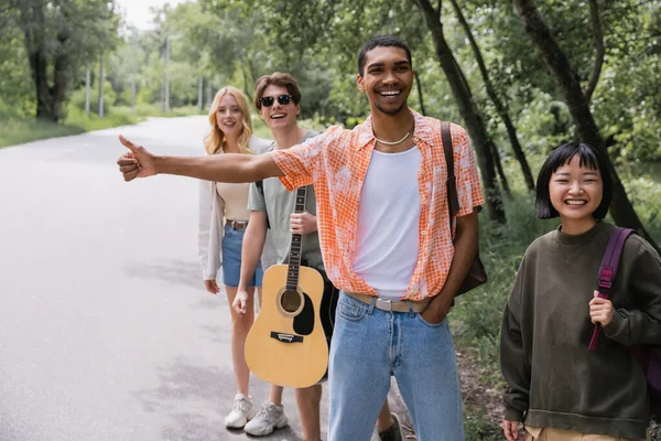 Cheerful interracial hitchhikers stopping car on countryside road — Stock Photo