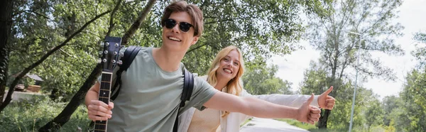 Young and cheerful hitchhikers with thumbs up stopping car in countryside, banner — Fotografia de Stock