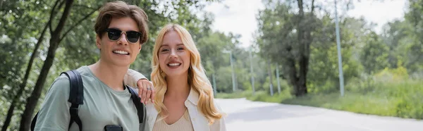 Young and happy travelers smiling at camera in countryside on summer day, banner — Stock Photo