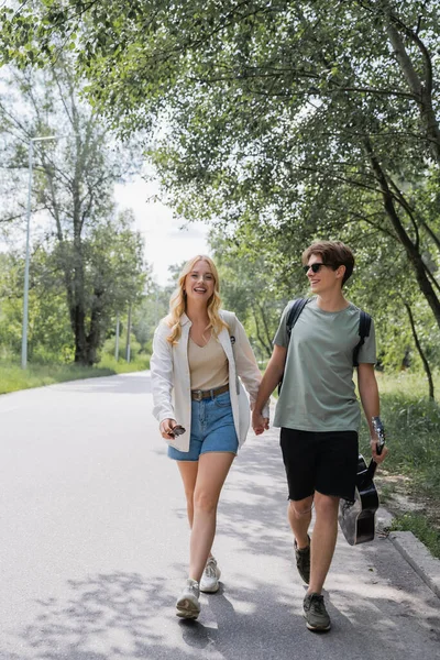 Full length of young travelers holding hands and walking on road along forest — Fotografia de Stock