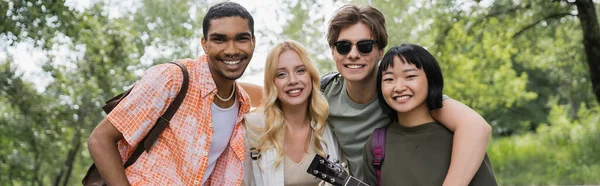 Young and cheerful multiethnic tourists looking at camera in countryside, banner — Fotografia de Stock