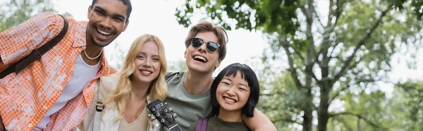 Young and cheerful multicultural travelers looking at camera outdoors, banner — Foto stock
