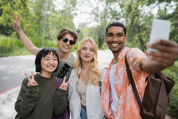 Happy african american man taking selfie with interracial friends showing victory signs — Photo de stock