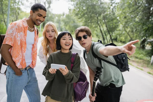 Man in sunglasses pointing direction with finger near multiethnic friends - foto de stock