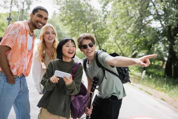 Man in sunglasses pointing with finger near asian woman with smartphone and happy interracial friends — Foto stock