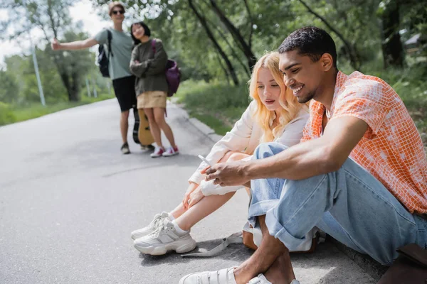 Smiling african american man searching route on smartphone near woman and blurred friends — Foto stock