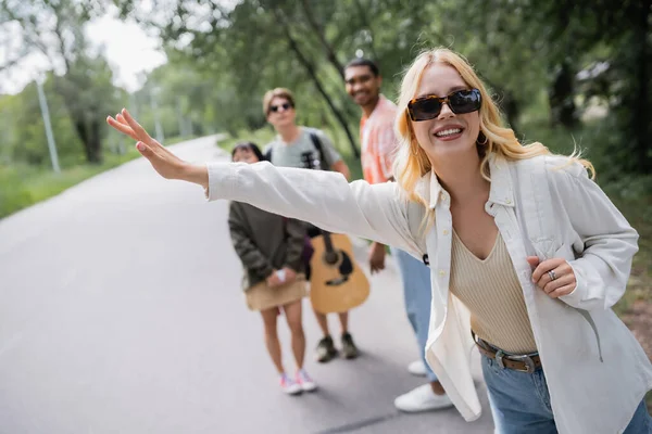 Blonde woman in sunglasses stopping car near blurred interracial hitchhikers — Stockfoto