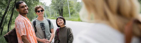Young multiethnic travelers smiling at woman on blurred foreground, banner — Stock Photo