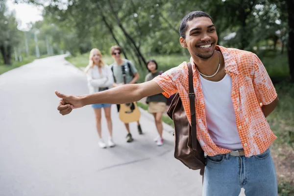 Cheerful african american man with thumb up stopping car near friends on blurred background — Fotografia de Stock