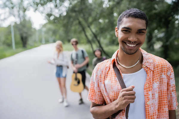 Young african american man smiling at camera near blurred travelers - foto de stock