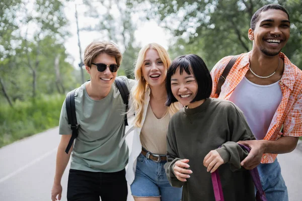 Excited multiethnic travelers with backpacks on road in countryside — Stock Photo