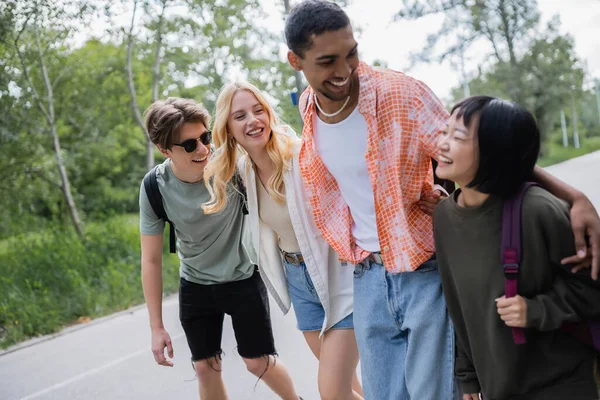 Cheerful multiethnic travelers embracing and laughing during summer walk in countryside — Photo de stock