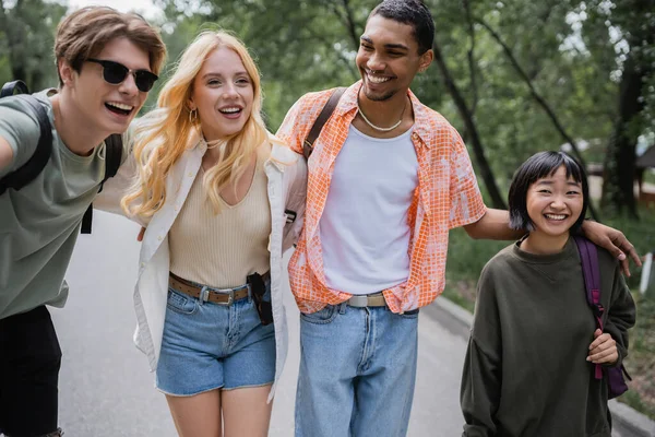 Young multiethnic friends embracing and laughing while traveling in countryside — Stock Photo