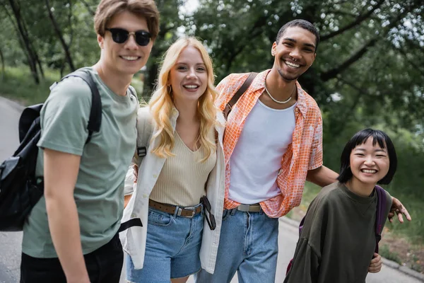 Happy multicultural travelers with backpacks smiling at camera outdoors - foto de stock