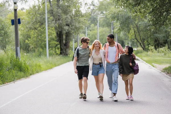 Full length of multicultural tourists embracing while walking on countryside road — Fotografia de Stock