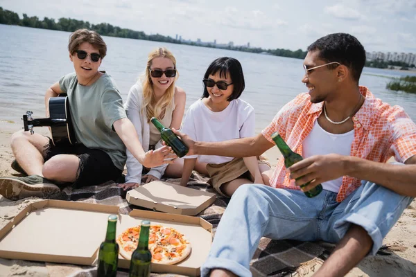 African american man giving beer to friend with guitar near interracial women — Stock Photo