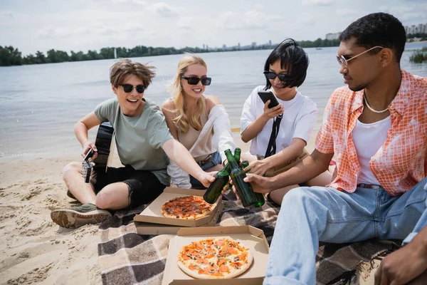 Asian woman taking photo on smartphone near friends clinking beer bottles — Fotografia de Stock