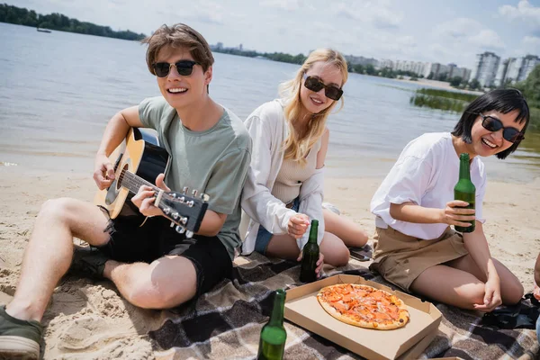 Happy man playing guitar near happy interracial women during beach party — Fotografia de Stock