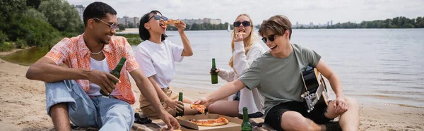 Multicultural friends in sunglasses drinking beer and eating pizza on beach party, banner — Fotografia de Stock