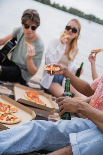 Blurred multiethnic friends eating pizza and drinking beer on beach party — Stock Photo