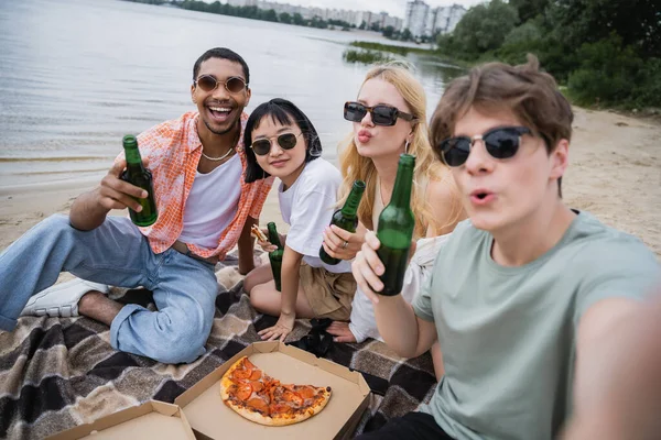 Interracial friends in sunglasses holding beer near tasty pizza on beach — Fotografia de Stock