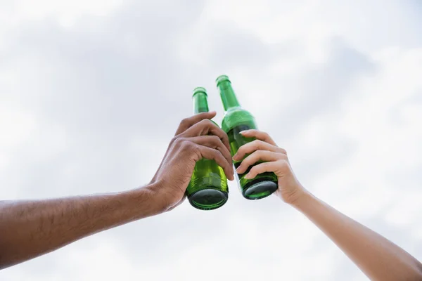 Low angle view of cropped interracial friends clinking beer bottles — Stock Photo