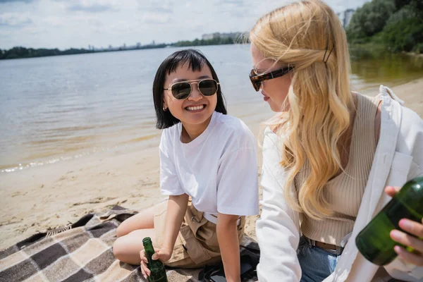 Smiling asian woman looking at blonde friend during picnic on beach — Fotografia de Stock