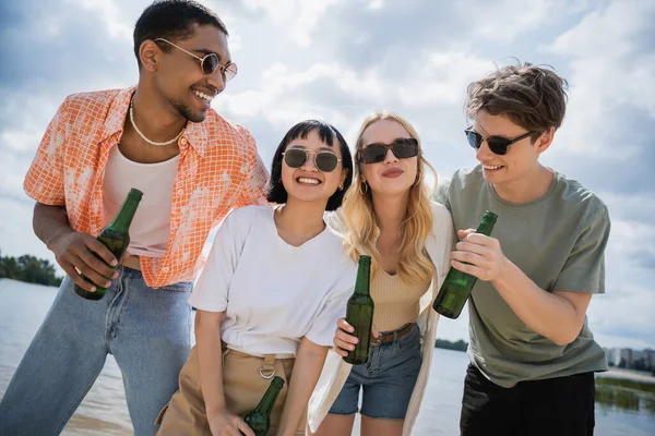 Young multicultural friends smiling while holding beer on beach — Stock Photo