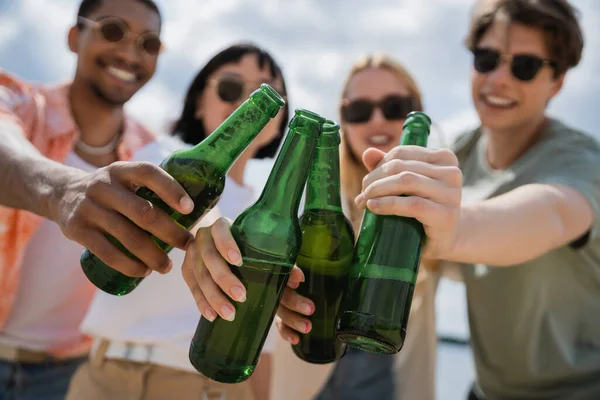 Blurred multicultural friends clinking bottles with fresh beer outdoors — Stock Photo