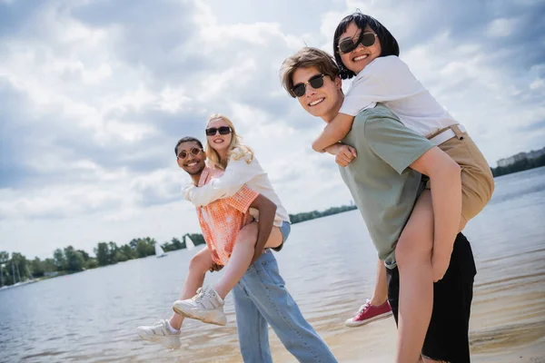 Happy multiethnic friends in sunglasses looking at camera while having fun on beach — Foto stock